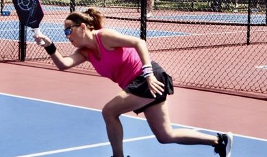 Woman on a pickleball court hits a ball 