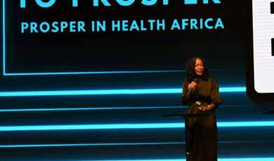  A woman stands in front of a sign that reads Equipped to Prosper holding a microphone 