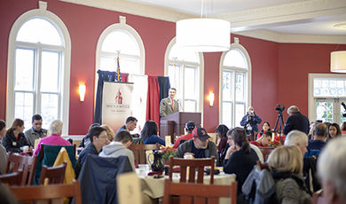 Students and parents sit at round tables in Flynn Dining Commons listening to a speaker.
