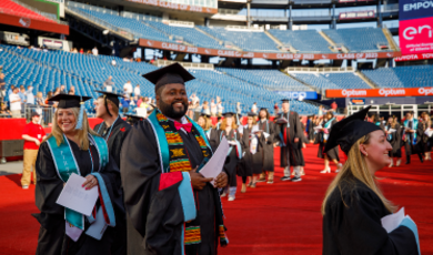 Graduates wearing caps and gowns walk towards the stage 