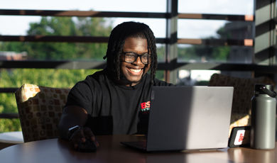 A man sits in front of a computer screen and is smiling 