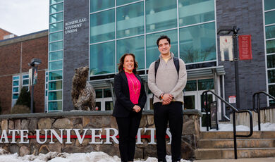 A woman and man stand smiling in front of a Bear Statue 