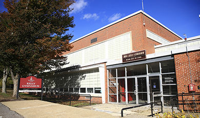 The exterior of Kelly Gymn, with trees and a sidewalk in the foreground.