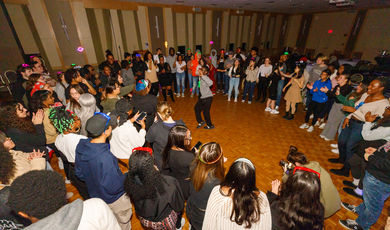  A large group of people dances around a man who is dancing in the middle 