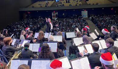 Musicians sit on a stage and look up at the conductor 