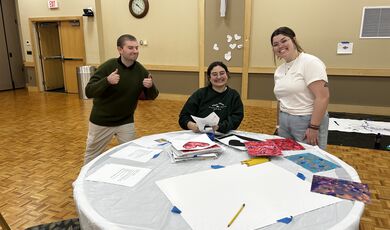 A group of people are at a table painting and smiling 