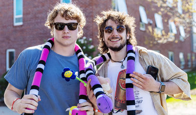 Two students wearing sunglasses and wearing toy snakes around their necks at Carnival