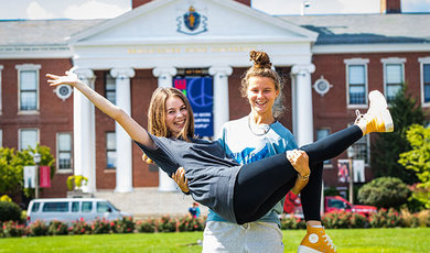 One student holds up another in her arms on Boyden Quad