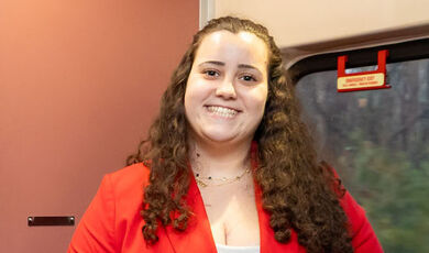 Sophia Penarreta smiling with long brown curly hair wearing a red pantsuit with a white top underneath