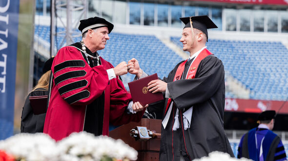 A smiling male BSU student fist bumps with President Clark as he is handed his diploma