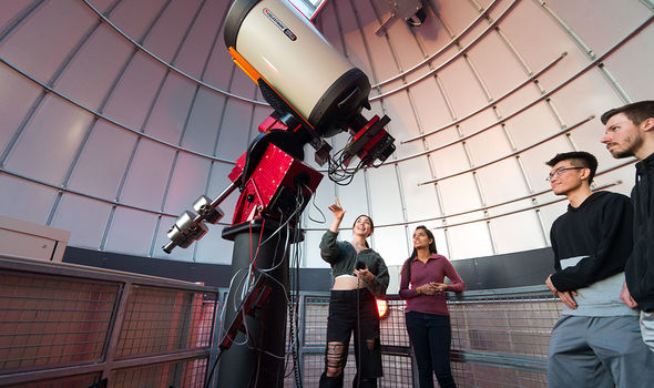 A student points at the telescope in the BSU Observatory as three more students look on