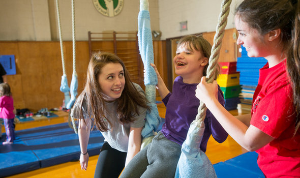 2 BSU students helping a child swing on a rope in a gym