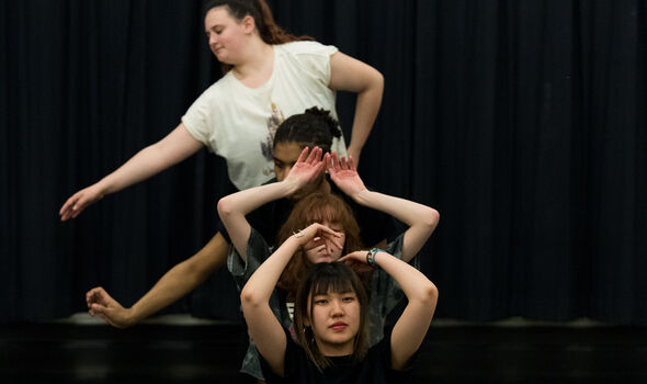 Four students dance in front of a black curtain