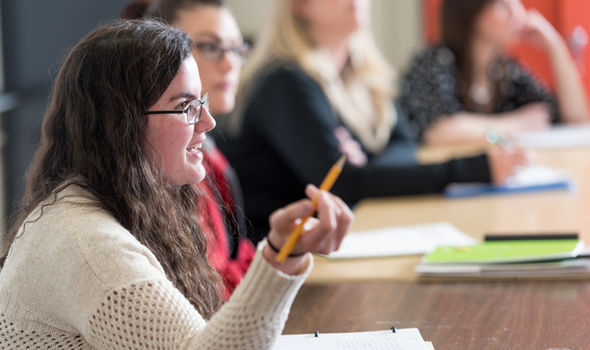 side view of a female BSU student with long dark brown hair and black wire rim glasses speaking, holding a pencil, sitting at a table with 3 other students