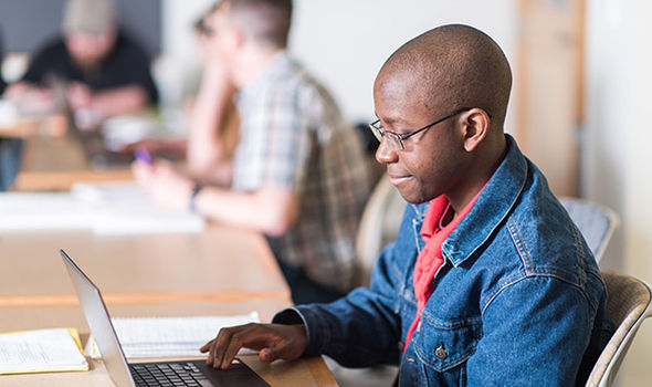 a BSU student sitting at a classroom table smiling as he works on his laptop