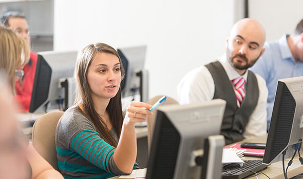 a BSU student in management class sits at a desk behind a computer and points a highlighter while speaking. Classmates look on.