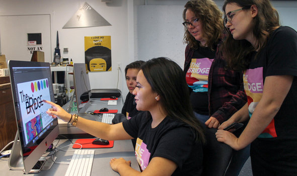 four students gathered around a computer looking at a cover design for The Bridge