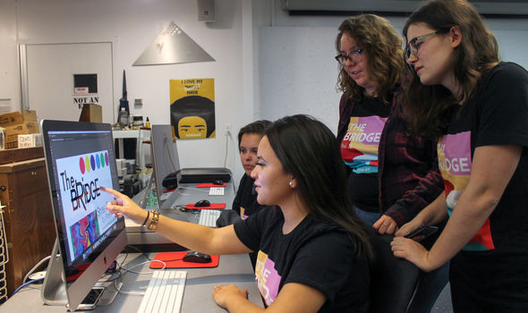 Four students gathered around a computer, discussing the cover for The Bridge