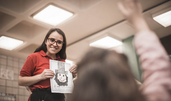 BSU TESOL student teacher smiling while holding up a drawing of Abraham Lincoln with a sentence under it in front of an elementary age student with her hand raised