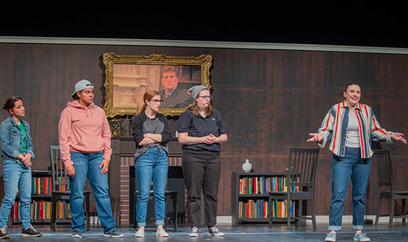 Five BSU students performing on RSU Auditorium stage with a backdrop of a paneled room with fireplace and bookcases