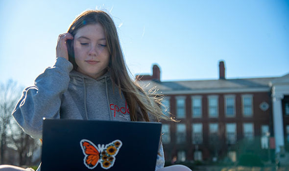 A BSU student sits on the grass on Boyden Quad working on her laptop