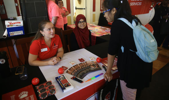 2 students sit behind a table with materials on it talking to another student leaning over the table. There is a Transfer Services sign next to the table.