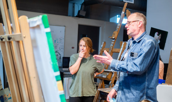 Dr. Collin Asmus and a student looking at and discussing a painting sitting on an easel