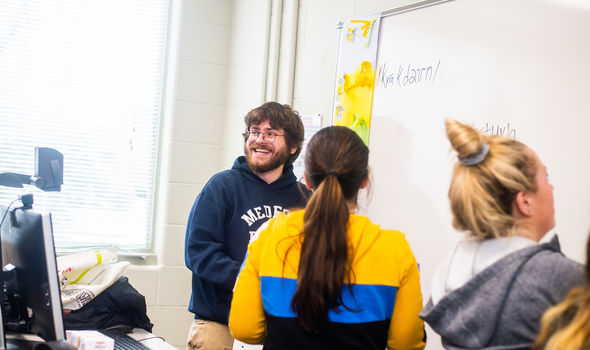 a student smiles looking at classroom from white board while 2 other students work at the board