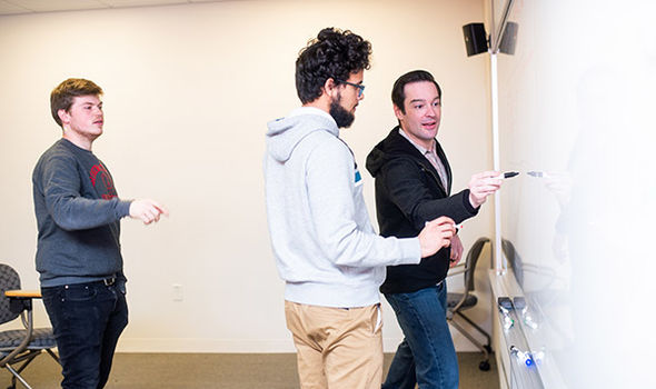 Professor Matt Salomone showing 2 students something on a whiteboard