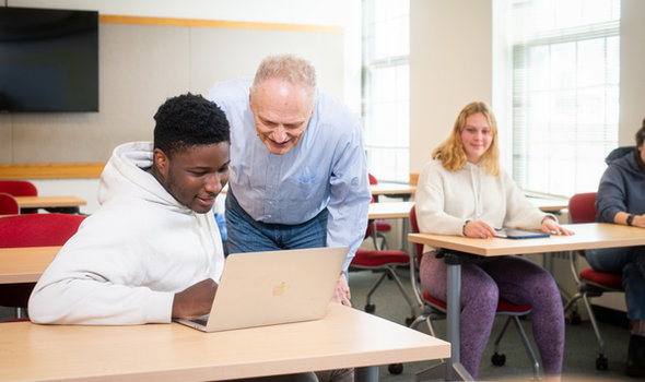A professor leaning over to help a student working on a laptop in the classroom