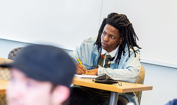 A student listens intently in class while taking notes