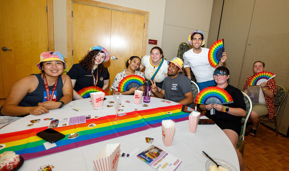 students holding rainbow fans sitting around a table decorated with a rainbow table runner