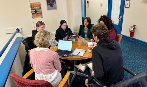 A professor and six students sitting working together at a round table