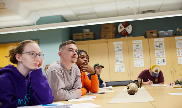 Students sitting at a classroom table with a skull and bones on the table listening to the class professor