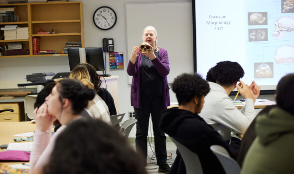 Dr. Ellen Ingmanson speaking at front of class while holding a skull next to a projector screen