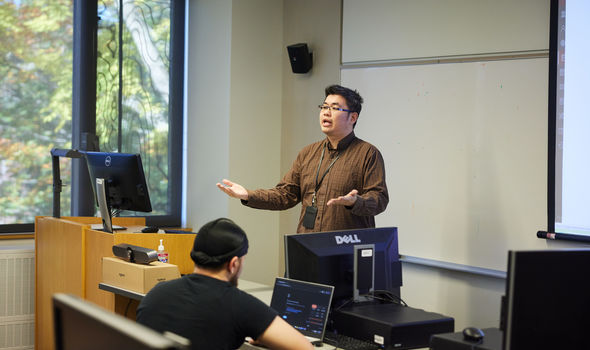 Dr. Cory Yeo teaching at the front of the class with a student at the front desk working on a laptop
