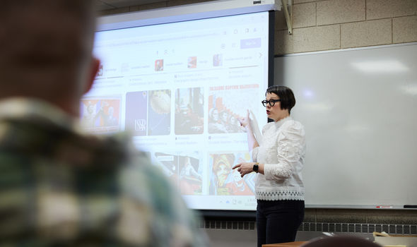 Dr. Melanie McNaughton points to images on a projector screen as she teaches at the front of classroom