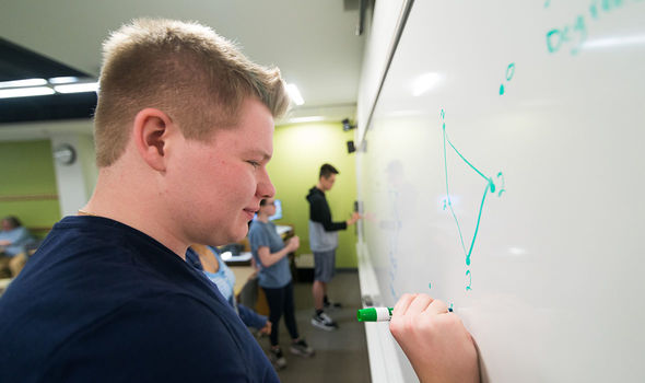 A student works out a math problem on a whiteboard in class