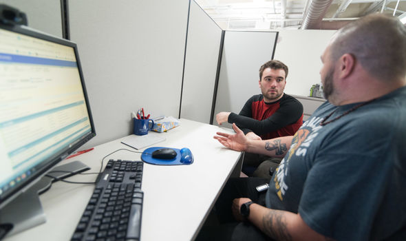 an advisor sits at a desk in front of a computer talking to a student sitting next to him