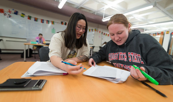 2 female students sit at a table in the Academic Achievement Center working together over papers