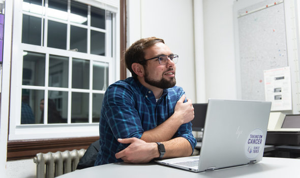 a male BSU student with glasses and short dark brown hair, mustache and beard looking up from his laptop