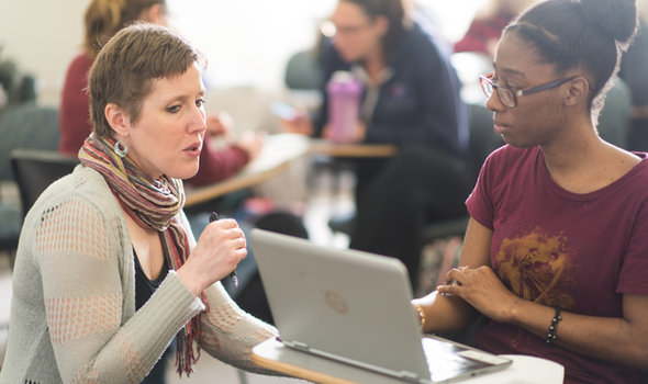 professor helping a student at a desk with a laptop open