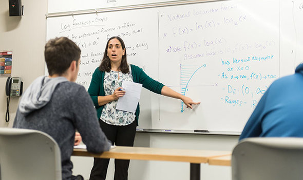 Dr. Rachel Stahl teaching class and pointing to a graph on a white board while students look on