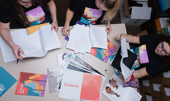 View from above a table where 3 BSU students review writing to include in The Bridge publication