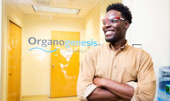 Claudio Eshun stands smiling with his safety glasses on in the office of Organogenesis, where he completed a summer internship.