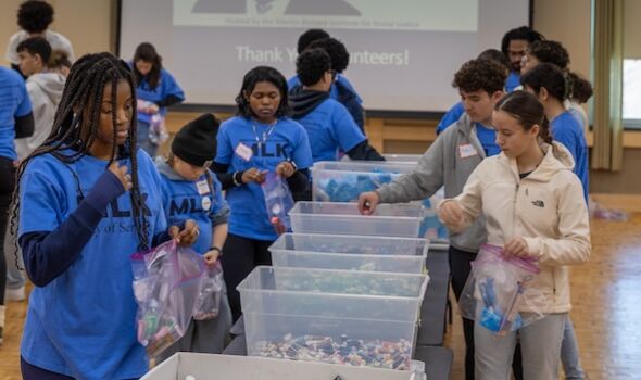 students and community members in blue MLK Day of Service t-shirts come together to pack hygiene supplies into comfort kits with Project PACK