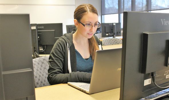 a BSU student working on her laptop in a classroom surrounded by computers