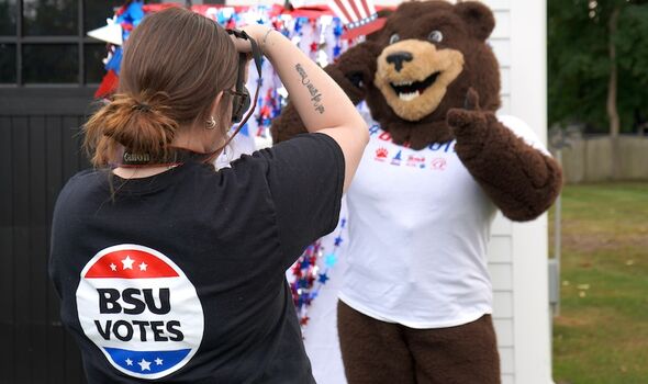 a female student wearing a black BSU Votes t-shirt holds a camera and takes a photo of Bristaco posing with voting themed props