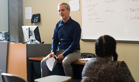Dr. Matt Bell sitting on a desk teaching an English class