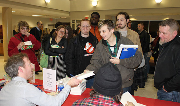 A group of students standing in front of of a table getting books autographed by visiting author Paul Murray